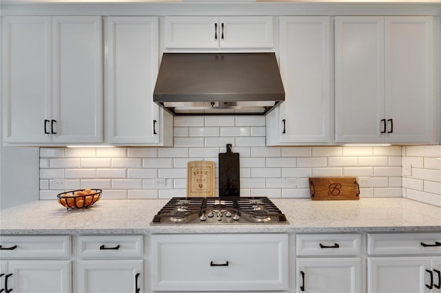 kitchen with light stone counters, under cabinet range hood, white cabinetry, tasteful backsplash, and stainless steel gas stovetop