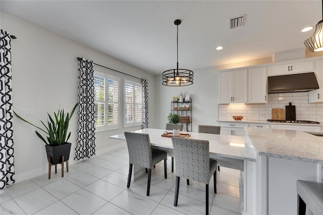 kitchen featuring light stone countertops, decorative backsplash, white cabinetry, and under cabinet range hood