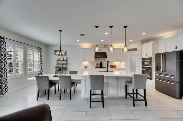 kitchen with high end refrigerator, white cabinets, decorative backsplash, under cabinet range hood, and double oven