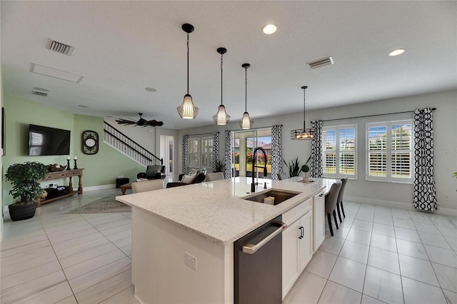 kitchen featuring visible vents, an island with sink, decorative light fixtures, stainless steel dishwasher, and a sink