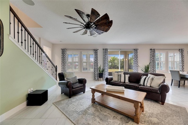 living area featuring a textured ceiling, a ceiling fan, baseboards, stairway, and tile patterned floors