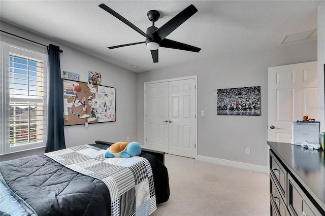 bedroom with a closet, light colored carpet, ceiling fan, a textured ceiling, and baseboards