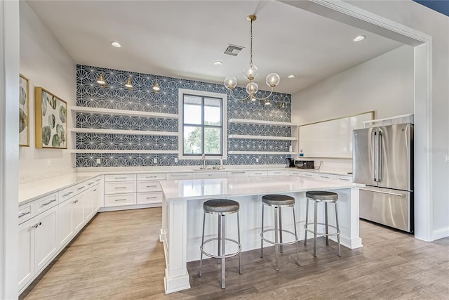 kitchen with open shelves, visible vents, freestanding refrigerator, white cabinets, and a sink