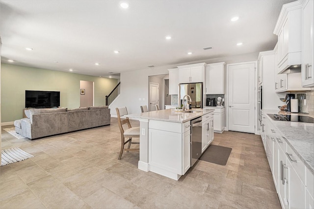 kitchen featuring stainless steel appliances, open floor plan, white cabinets, an island with sink, and a kitchen bar