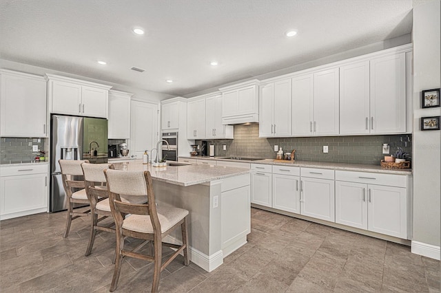 22990 Scaglione Dr, Lutz, FL 33549 - kitchen featuring appliances with stainless steel finishes, white cabinetry, backsplash, a breakfast bar area, and a center island with sink