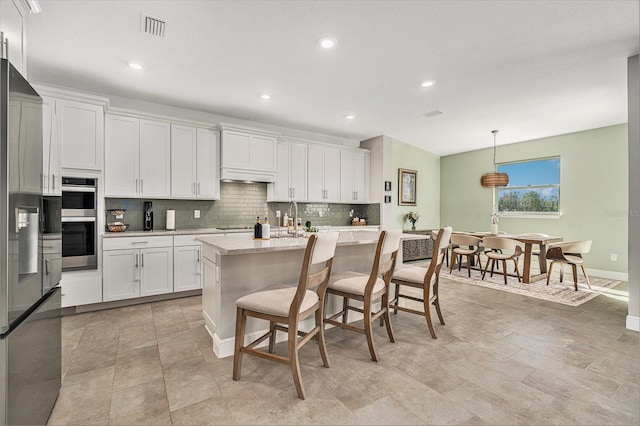 22990 Scaglione Dr, Lutz, FL 33549 - kitchen featuring backsplash, appliances with stainless steel finishes, custom range hood, white cabinets, and an island with sink