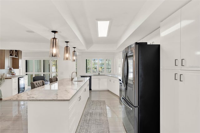 kitchen featuring stainless steel refrigerator, white cabinetry, a kitchen bar, a kitchen island with sink, and a raised ceiling