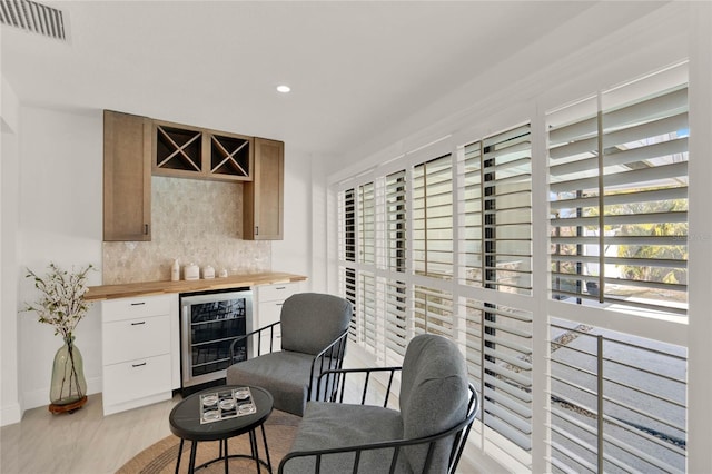 interior space featuring wine cooler, butcher block counters, white cabinetry, light wood-type flooring, and backsplash