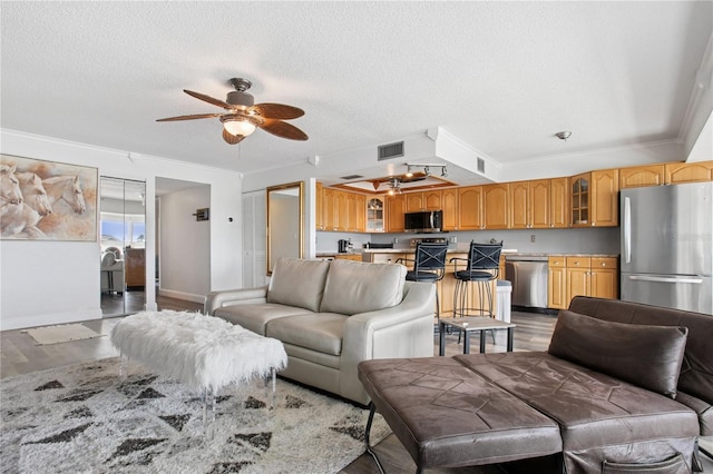living area with a textured ceiling, wood finished floors, ceiling fan, and ornamental molding