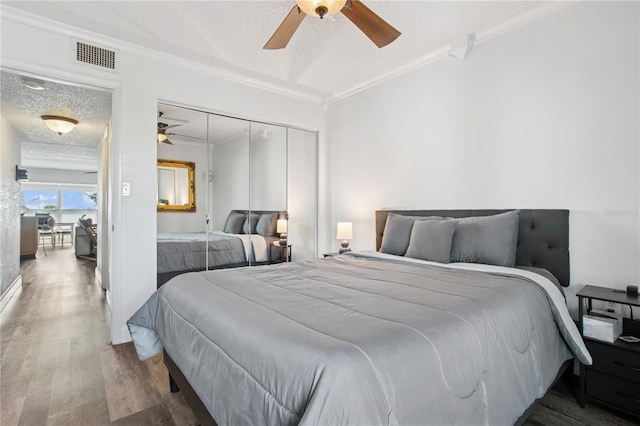 bedroom with a textured ceiling, crown molding, visible vents, ceiling fan, and wood finished floors