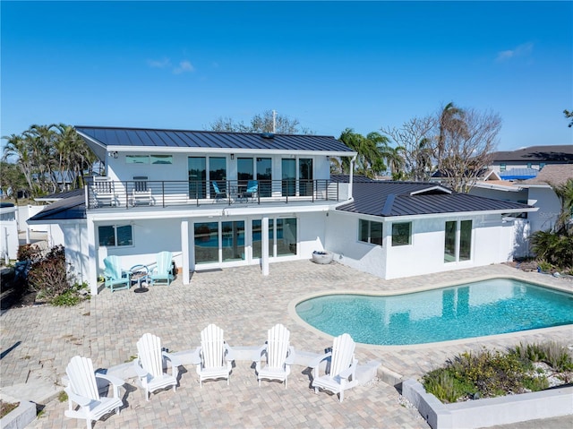 rear view of property featuring a balcony, a standing seam roof, a patio, and stucco siding