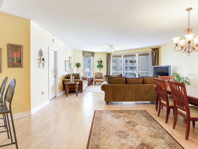 living room with light wood finished floors, baseboards, a textured ceiling, and ceiling fan with notable chandelier