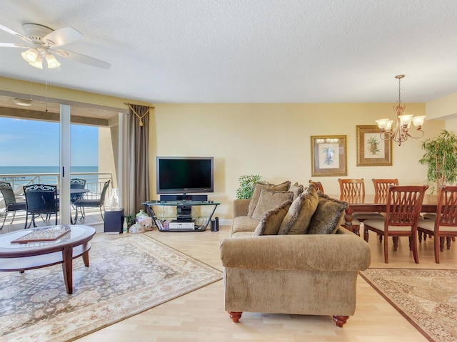 living room with light wood-style flooring, a textured ceiling, and ceiling fan with notable chandelier