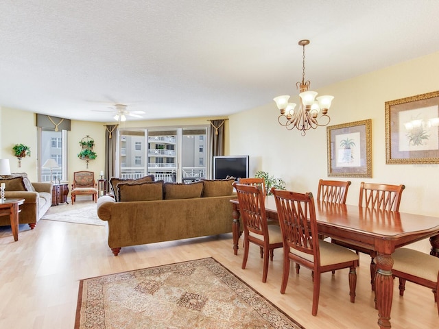 dining room featuring light wood-type flooring, a textured ceiling, and ceiling fan with notable chandelier