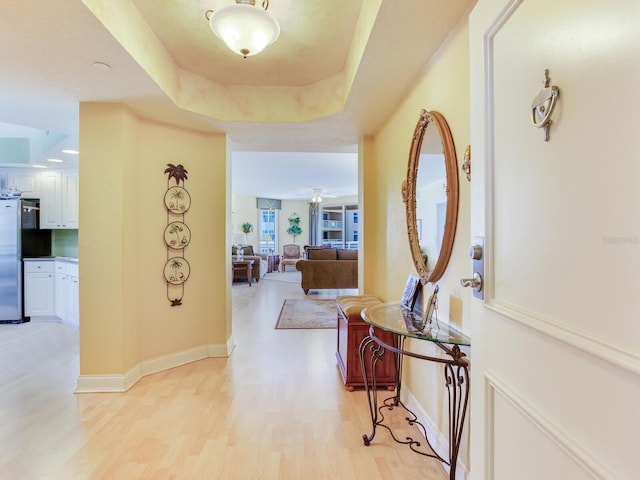 hallway with light wood finished floors, baseboards, and a raised ceiling