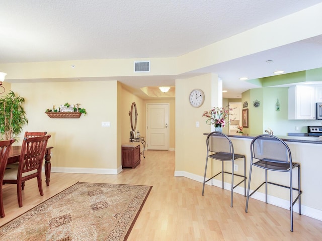 kitchen with a kitchen bar, visible vents, white cabinets, light wood-type flooring, and baseboards