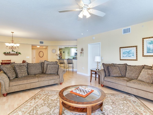 living area with a textured ceiling, light wood finished floors, ceiling fan with notable chandelier, and visible vents