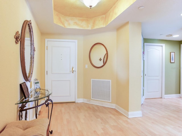 entrance foyer featuring baseboards, a tray ceiling, visible vents, and light wood-style floors