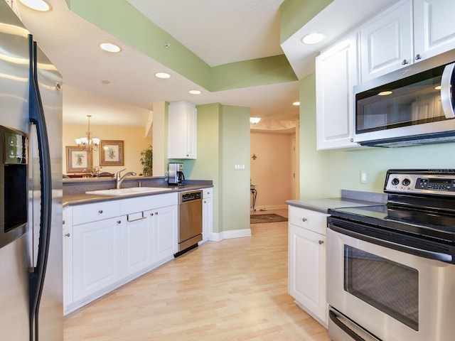 kitchen featuring light wood finished floors, white cabinets, appliances with stainless steel finishes, decorative light fixtures, and a sink