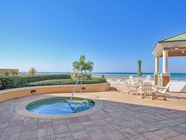 view of swimming pool featuring a water view, a patio area, a hot tub, and a beach view