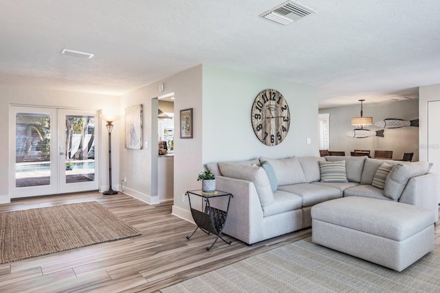 living room featuring a textured ceiling, light wood-type flooring, and french doors