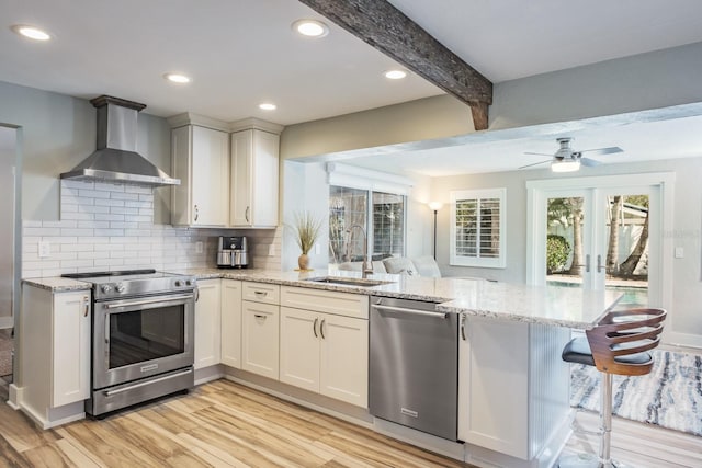 kitchen with sink, kitchen peninsula, stainless steel appliances, light stone countertops, and wall chimney exhaust hood