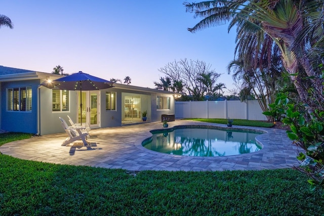 pool at dusk featuring a lawn and a patio area