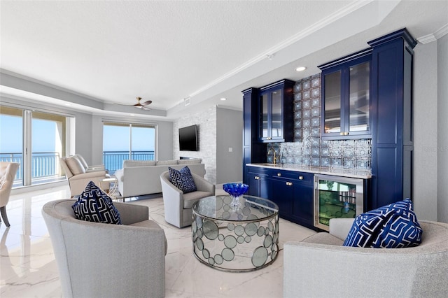 living room with wine cooler, marble finish floor, a tray ceiling, a textured ceiling, and wet bar