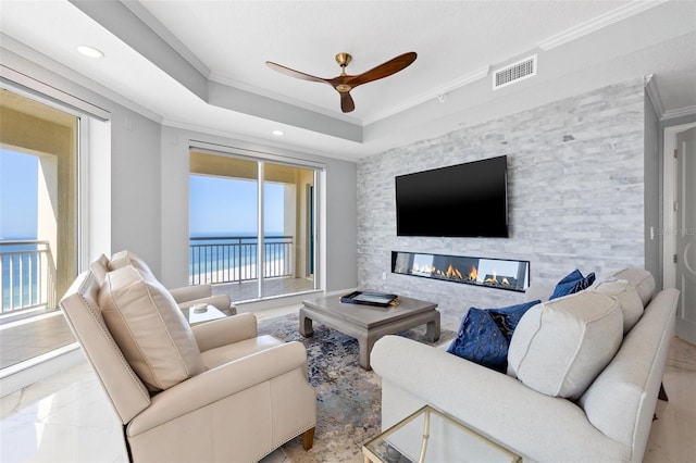 living room featuring a fireplace, a ceiling fan, visible vents, a tray ceiling, and crown molding