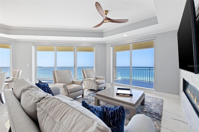 living area featuring a tray ceiling, marble finish floor, crown molding, a fireplace with flush hearth, and baseboards