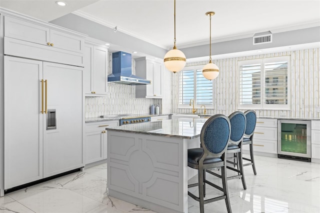 kitchen featuring wine cooler, ornamental molding, marble finish floor, paneled built in refrigerator, and wall chimney range hood