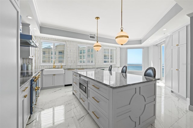 kitchen with a sink, a kitchen island, marble finish floor, stainless steel microwave, and a raised ceiling