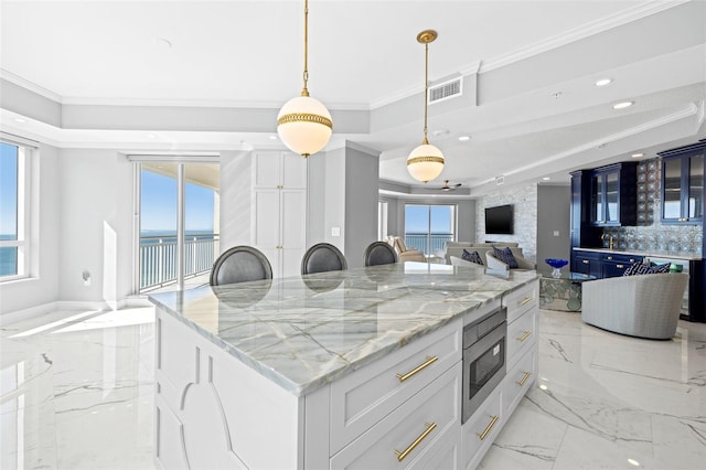 kitchen with visible vents, a kitchen island, stainless steel microwave, ornamental molding, and marble finish floor