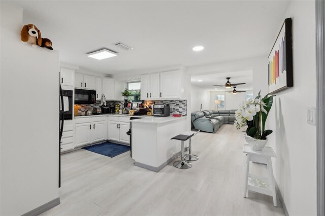 2419 Palmwood Dr, Holiday, FL 34690 - kitchen with white cabinetry, tasteful backsplash, a kitchen bar, kitchen peninsula, and light wood-type flooring