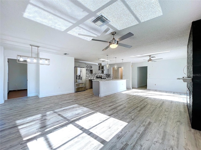 8600 Berkley Dr, Hudson, FL 34667 - kitchen featuring ceiling fan with notable chandelier, a textured ceiling, stainless steel fridge, and light wood-type flooring