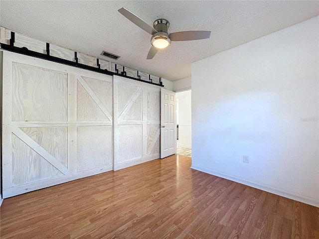 8600 Berkley Dr, Hudson, FL 34667 - unfurnished bedroom featuring ceiling fan, hardwood / wood-style flooring, a barn door, and a textured ceiling