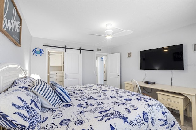 bedroom featuring ceiling fan, a barn door, and hardwood / wood-style flooring