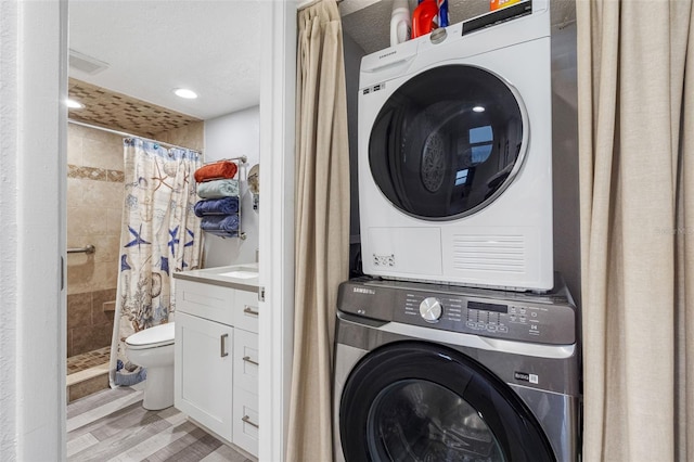 clothes washing area featuring stacked washer and dryer, light wood-type flooring, and a textured ceiling