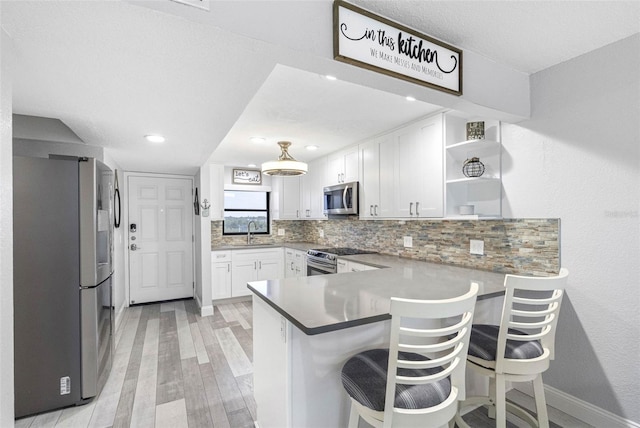 kitchen with appliances with stainless steel finishes, a kitchen breakfast bar, white cabinets, decorative backsplash, and kitchen peninsula