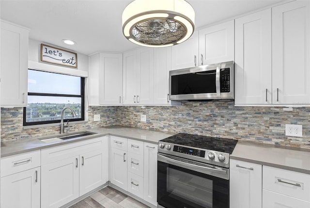 kitchen featuring appliances with stainless steel finishes, tasteful backsplash, white cabinets, light hardwood / wood-style floors, and sink