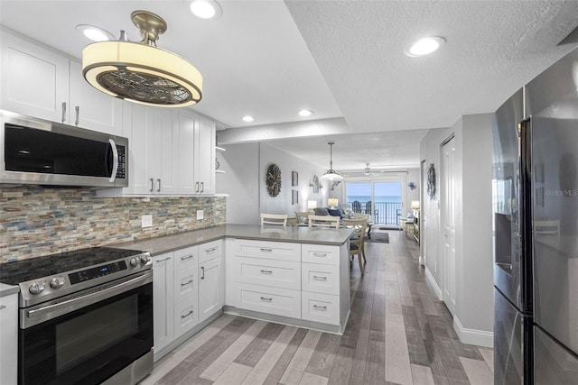 kitchen with hanging light fixtures, appliances with stainless steel finishes, white cabinetry, and kitchen peninsula