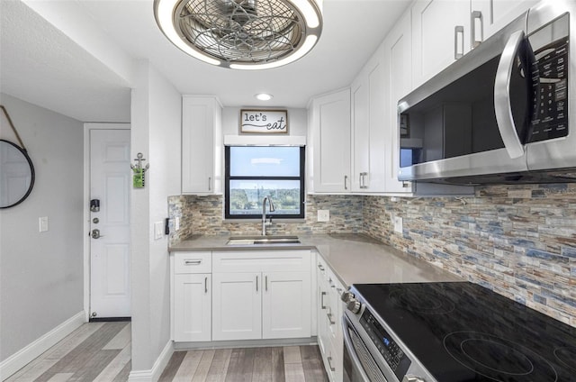 kitchen featuring white cabinetry, light wood-type flooring, sink, backsplash, and appliances with stainless steel finishes