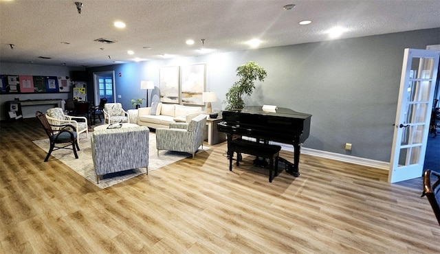 living area featuring light wood-type flooring, visible vents, a textured ceiling, and baseboards