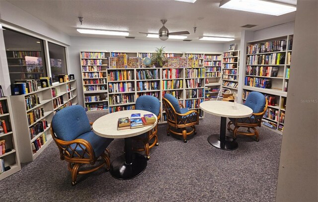 sitting room with a textured ceiling, carpet floors, visible vents, a ceiling fan, and bookshelves