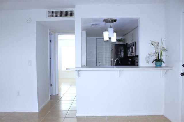 kitchen with fridge, decorative light fixtures, kitchen peninsula, and light tile patterned flooring