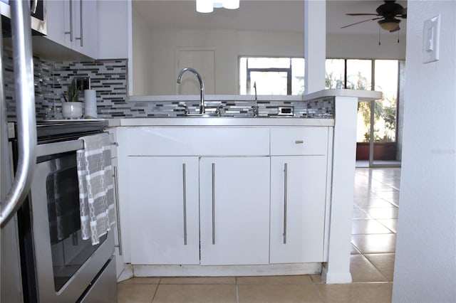 kitchen with tasteful backsplash, range, white cabinets, and light tile patterned floors