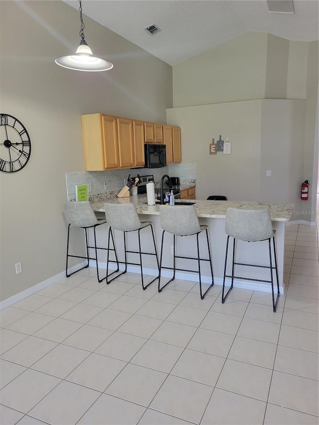 kitchen with a breakfast bar area, tasteful backsplash, light brown cabinetry, decorative light fixtures, and kitchen peninsula