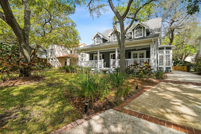 new england style home featuring a porch, ceiling fan, and a front lawn