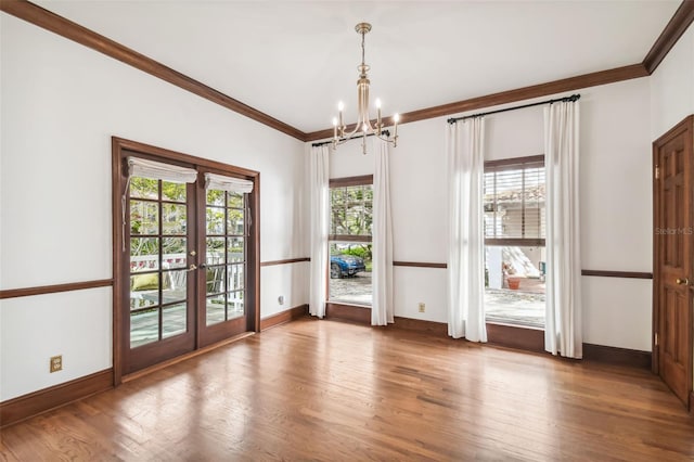 empty room with french doors, a notable chandelier, crown molding, and hardwood / wood-style flooring