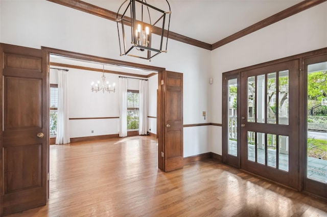 foyer entrance with crown molding, light wood-type flooring, and a notable chandelier